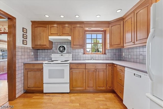 kitchen with light countertops, light wood finished floors, white appliances, and a sink