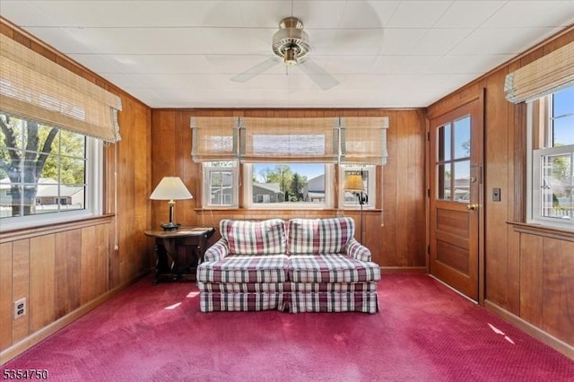 sitting room featuring baseboards, a ceiling fan, carpet, and wooden walls