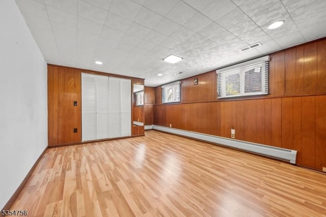 unfurnished room featuring visible vents, light wood-type flooring, baseboards, a baseboard radiator, and wooden walls
