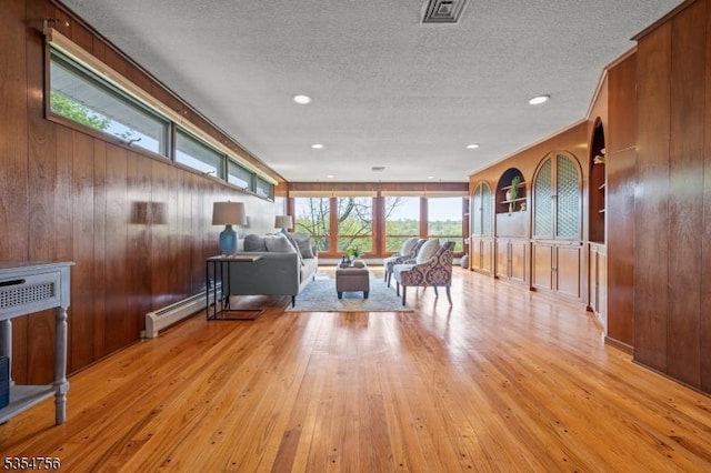 living room featuring visible vents, wood walls, light wood-type flooring, a textured ceiling, and a baseboard heating unit