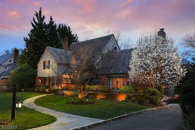tudor home with a lawn, brick siding, and a chimney