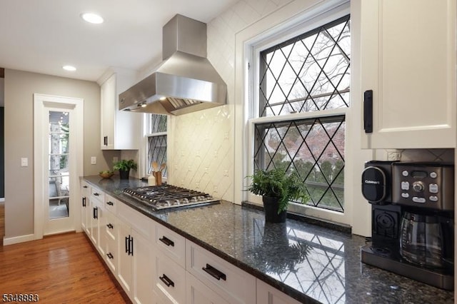 kitchen featuring light wood-type flooring, white cabinetry, stainless steel gas stovetop, dark stone counters, and extractor fan