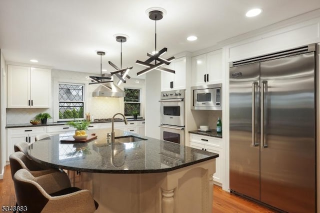 kitchen with a sink, built in appliances, backsplash, and light wood-type flooring