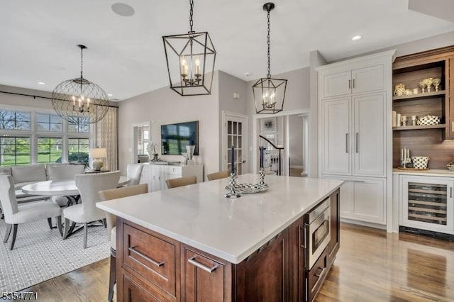 kitchen featuring stainless steel microwave, an inviting chandelier, wood finished floors, and wine cooler