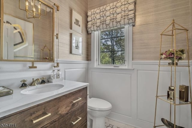 bathroom with toilet, wallpapered walls, a wainscoted wall, and vanity