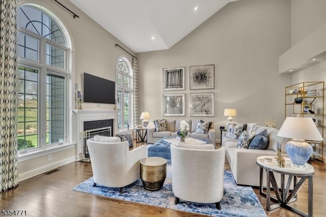 living room with a healthy amount of sunlight, high vaulted ceiling, a glass covered fireplace, and wood finished floors