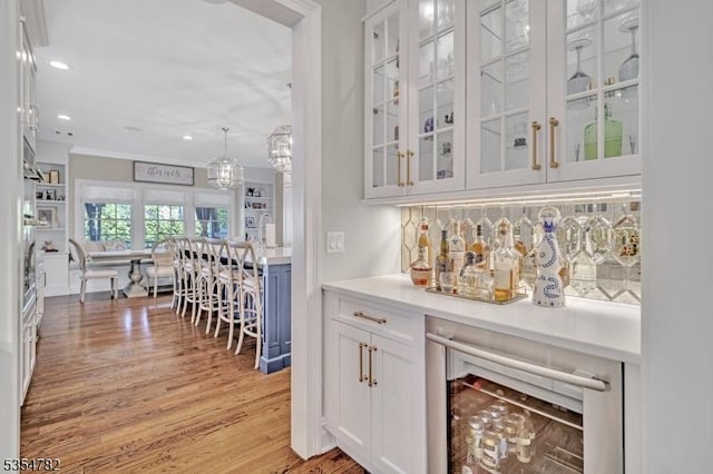 bar featuring crown molding, light wood finished floors, beverage cooler, recessed lighting, and backsplash