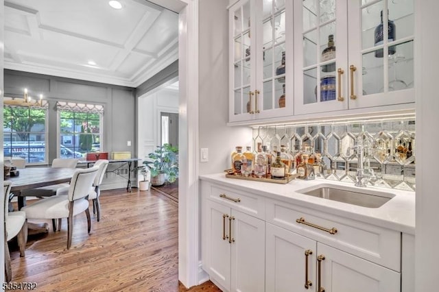 bar featuring light wood-style flooring, indoor wet bar, tasteful backsplash, ornamental molding, and coffered ceiling