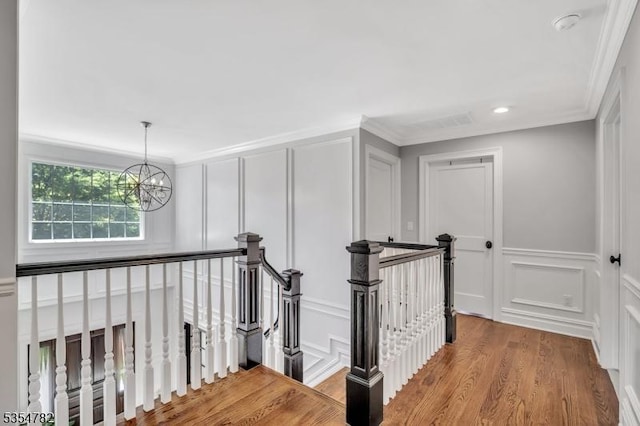 corridor with light wood-style flooring, a decorative wall, a notable chandelier, and an upstairs landing