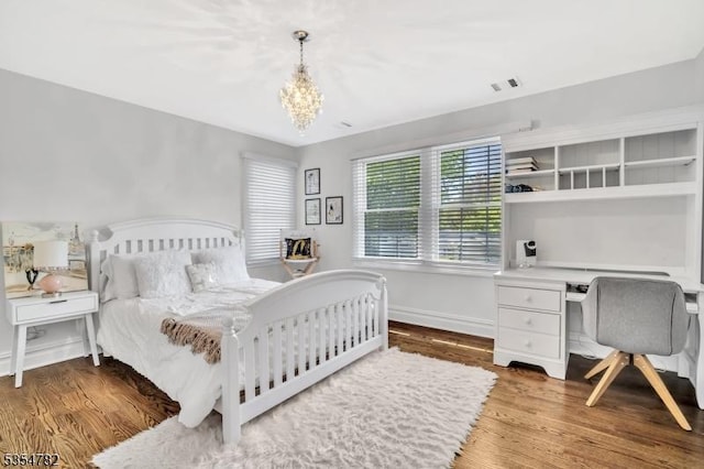 bedroom featuring visible vents, wood finished floors, built in study area, baseboards, and a chandelier