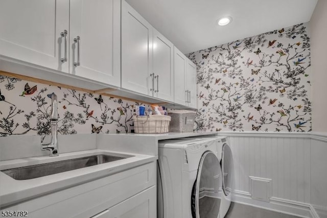 washroom featuring washer and dryer, wallpapered walls, a wainscoted wall, a sink, and cabinet space