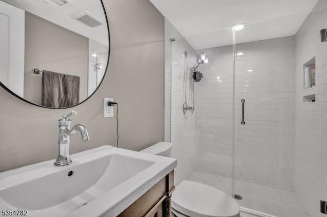 bathroom with vanity, a shower stall, toilet, and visible vents