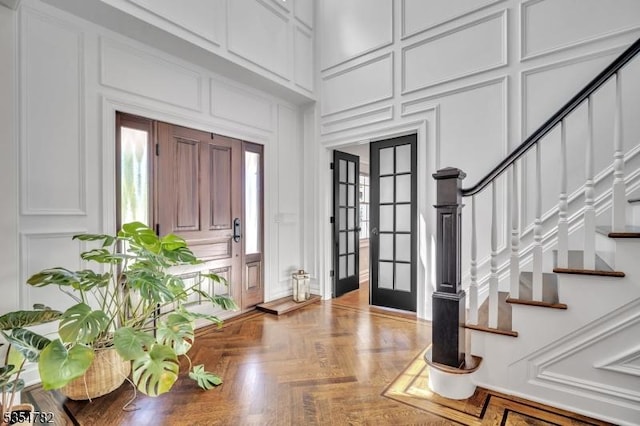 foyer entrance with french doors, a high ceiling, stairs, and a decorative wall