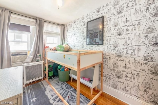 bedroom featuring cooling unit, radiator heating unit, baseboards, wallpapered walls, and wood finished floors
