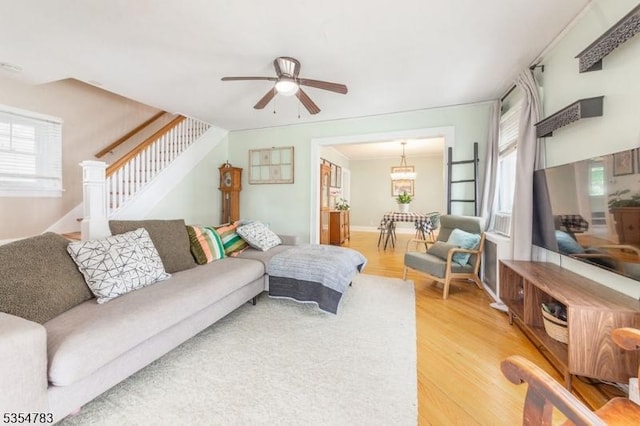 living area with stairway, a ceiling fan, and light wood finished floors