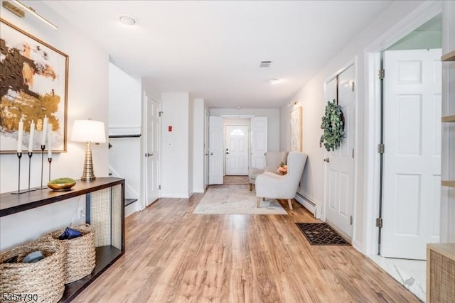 hall with baseboards, light wood finished floors, a baseboard heating unit, and visible vents
