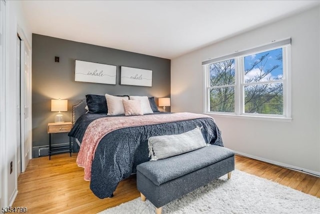bedroom with baseboards, a baseboard heating unit, and light wood-type flooring