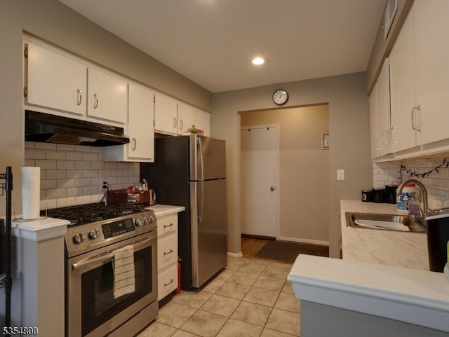 kitchen with a sink, under cabinet range hood, light countertops, appliances with stainless steel finishes, and tasteful backsplash