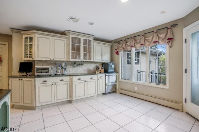 kitchen featuring dark countertops, tasteful backsplash, a baseboard heating unit, and cream cabinetry