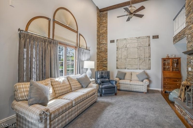 carpeted living area with ceiling fan, visible vents, high vaulted ceiling, baseboards, and beamed ceiling