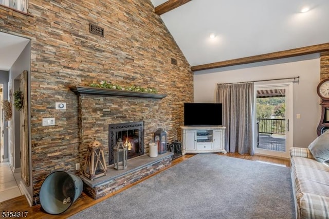 living room featuring visible vents, beam ceiling, wood finished floors, a stone fireplace, and high vaulted ceiling