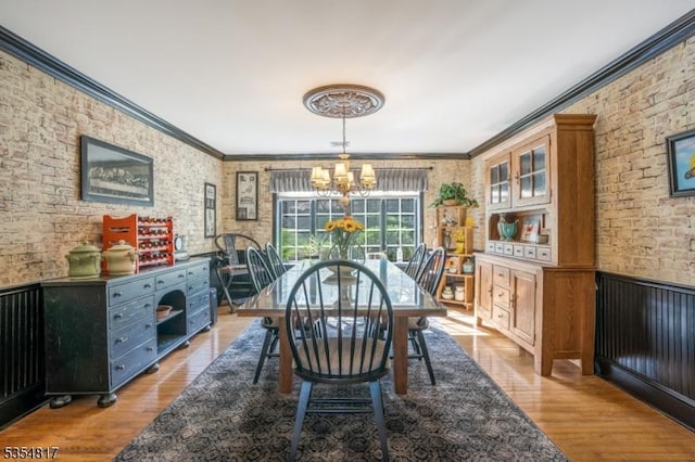 dining room featuring an inviting chandelier, ornamental molding, brick wall, and wood finished floors