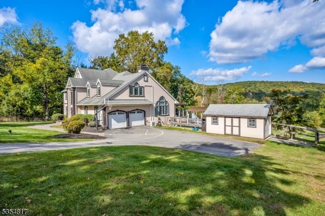 view of front of property featuring fence, aphalt driveway, a garage, a front yard, and an outdoor structure