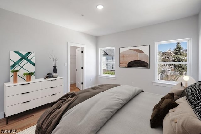 bedroom featuring a walk in closet, baseboards, recessed lighting, and light wood-style flooring