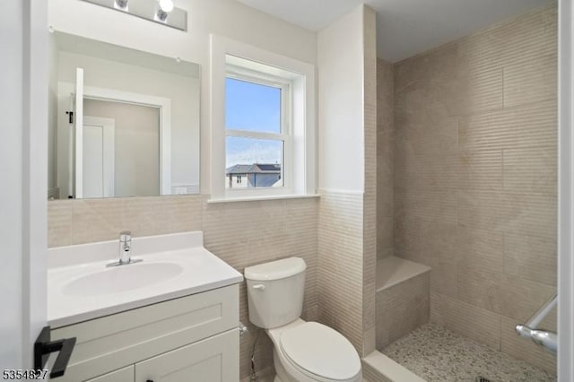 full bath featuring vanity, toilet, tile walls, a wainscoted wall, and a tile shower
