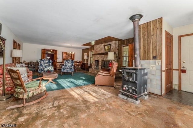 living area featuring a wood stove, concrete floors, a brick fireplace, and a notable chandelier