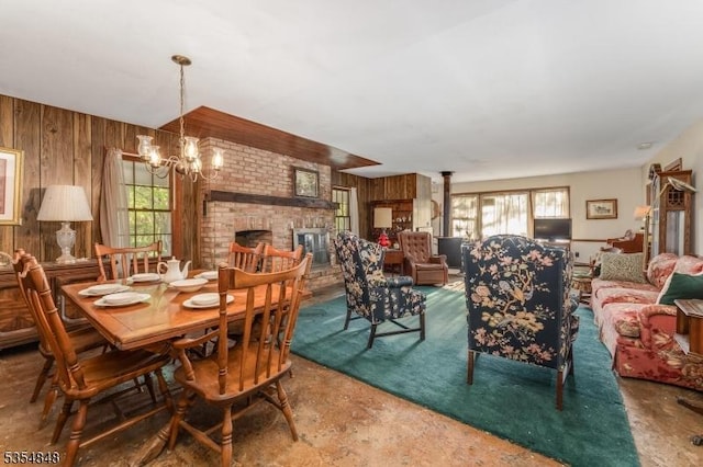 dining space featuring wooden walls, a brick fireplace, and a notable chandelier