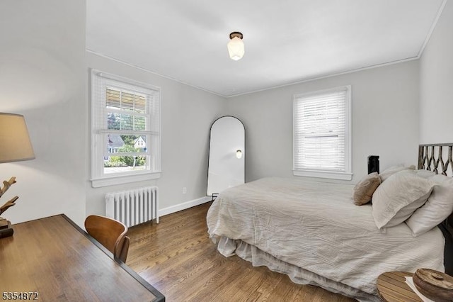 bedroom with radiator heating unit, wood finished floors, crown molding, and baseboards