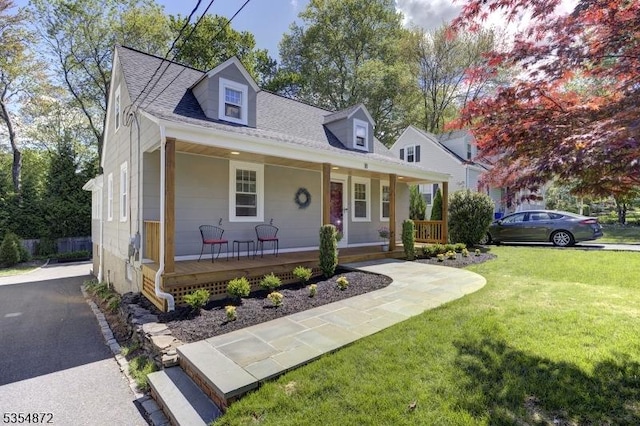 new england style home featuring covered porch, a front yard, and roof with shingles