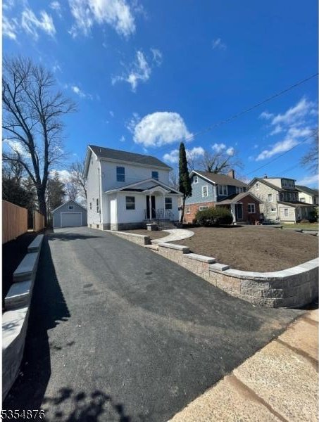 view of front of house with an outdoor structure, aphalt driveway, fence, a residential view, and a detached garage