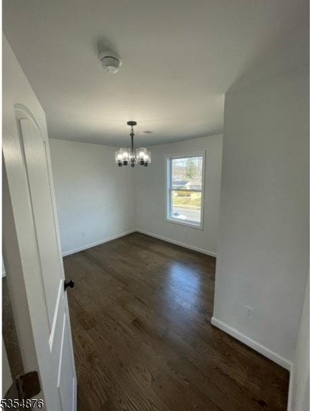 unfurnished dining area featuring an inviting chandelier, baseboards, and dark wood-type flooring