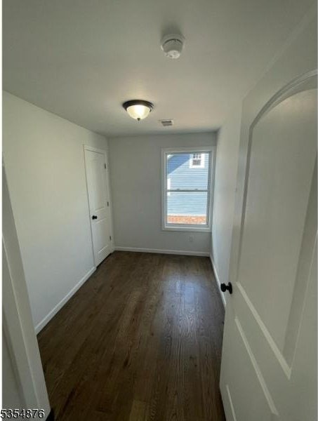 spare room featuring dark wood-type flooring and baseboards