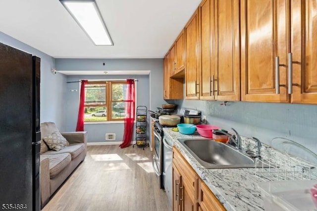 kitchen with brown cabinetry, visible vents, light wood-style floors, stainless steel gas range oven, and a sink