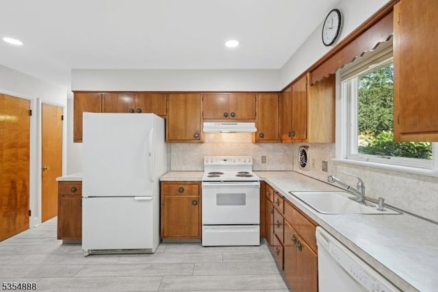 kitchen featuring a sink, white appliances, light countertops, brown cabinetry, and under cabinet range hood