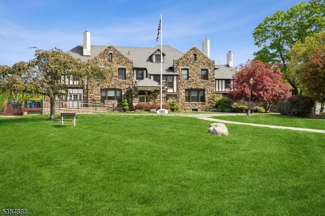 view of front facade featuring a chimney, stone siding, and a front lawn