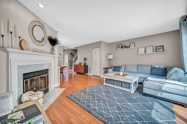 living area with a textured ceiling, recessed lighting, baseboards, wood finished floors, and a high end fireplace