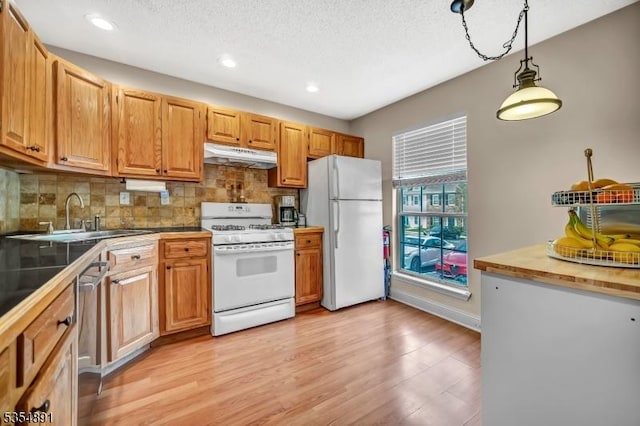 kitchen with a sink, white appliances, recessed lighting, backsplash, and under cabinet range hood