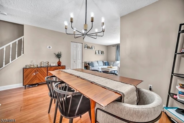 dining room featuring a notable chandelier, light wood-style floors, a textured ceiling, stairs, and baseboards