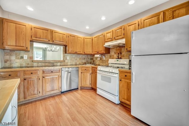 kitchen with light wood-type flooring, light countertops, under cabinet range hood, and white appliances