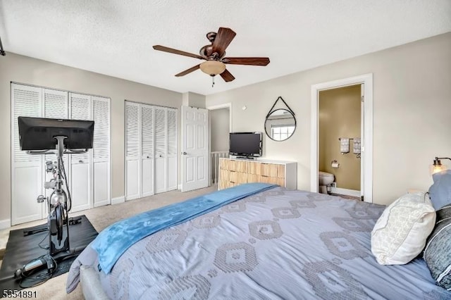 carpeted bedroom featuring multiple closets, ensuite bathroom, baseboards, and ceiling fan
