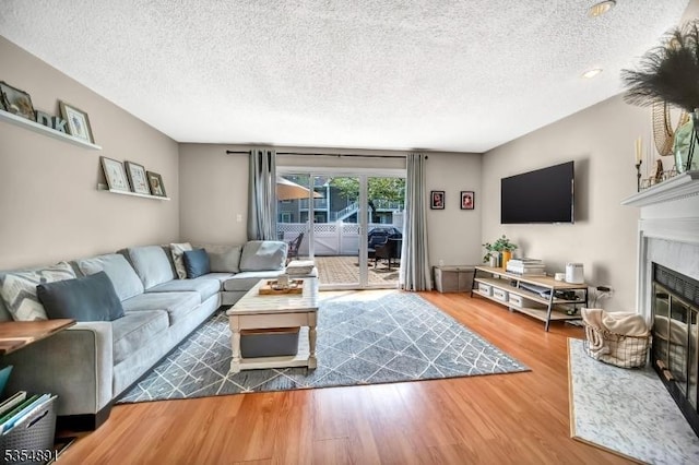 living room featuring a textured ceiling, a glass covered fireplace, and wood finished floors