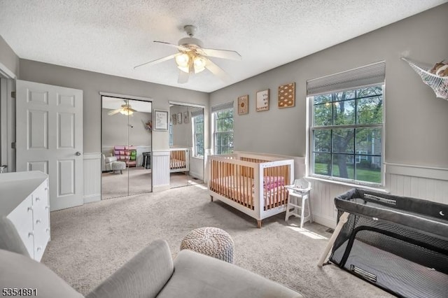 carpeted bedroom with a textured ceiling, multiple closets, wainscoting, and ceiling fan