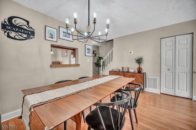 dining room with a textured ceiling, visible vents, wood finished floors, a notable chandelier, and stairs