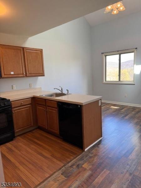kitchen with a peninsula, dark wood-type flooring, light countertops, a sink, and black appliances