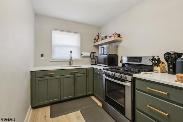 kitchen featuring open shelves, a sink, stainless steel gas range oven, light countertops, and green cabinets