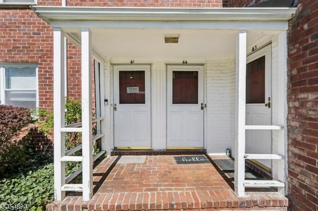 doorway to property featuring a porch and brick siding